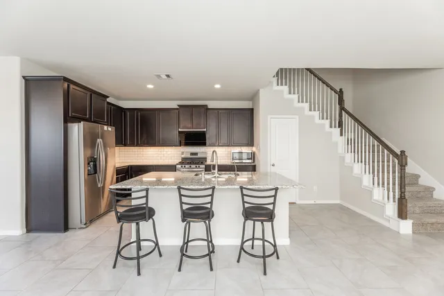 a kitchen with stainless steel appliances kitchen island granite countertop a refrigerator a stove a microwave oven with a dining table and chairs