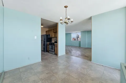 an empty room with kitchen and a chandelier fan