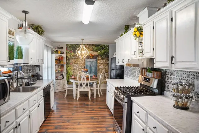 a kitchen with stainless steel appliances granite countertop a stove top oven a sink a dining table and chairs with wooden floor