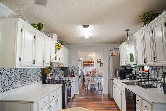 a kitchen with stainless steel appliances a stove a sink a refrigerator white cabinets and wooden floor