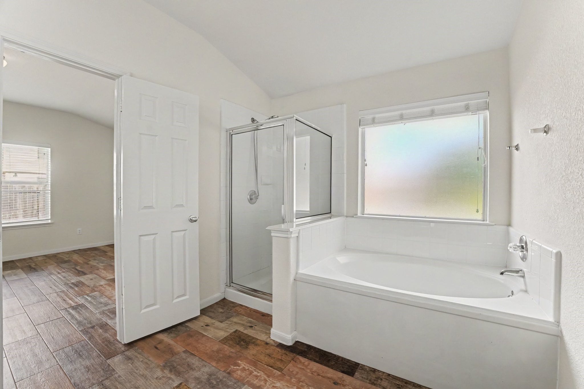 21427 Blooming Rock Lane Spring, TX 77379 - Photo 21 of 32 This bathroom features a large soaking tub, a separate glass-enclosed shower, and a frosted window for natural light. The space has a clean, white finish and leads into a room with wood-look tile flooring.