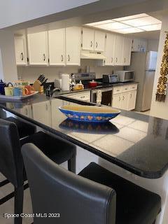1830 North Atlantic Avenue, Unit 205 Cocoa Beach, FL 32931 - Photo 6 of 28 a kitchen with stainless steel appliances granite countertop a sink a stove and white cabinets