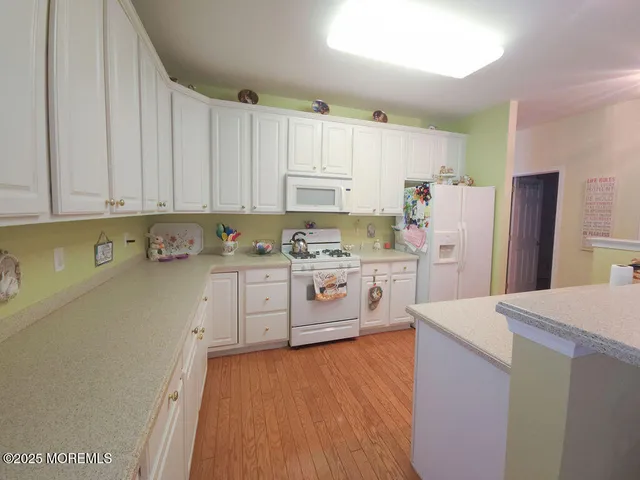 a kitchen with refrigerator a stove a sink and white cabinets with wooden floor
