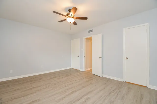 an empty room with wooden floor fan and windows