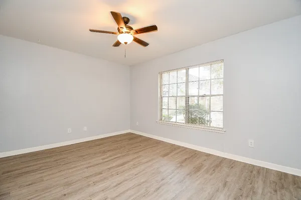 an empty room with wooden floor fan and windows