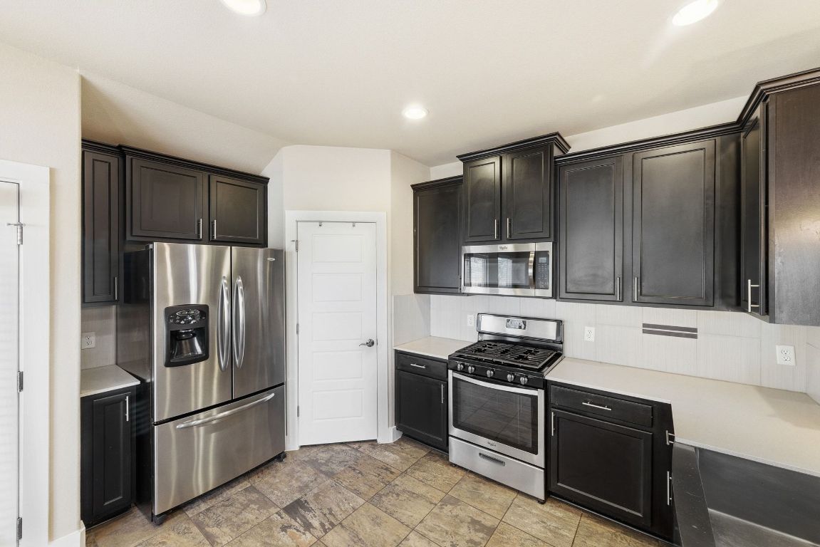 7013 Brick Slope Path Austin, TX 78744 - Photo 11 of 28 Kitchen with appliances with stainless steel finishes, light countertops, decorative backsplash, stone finish flooring, and recessed lighting
