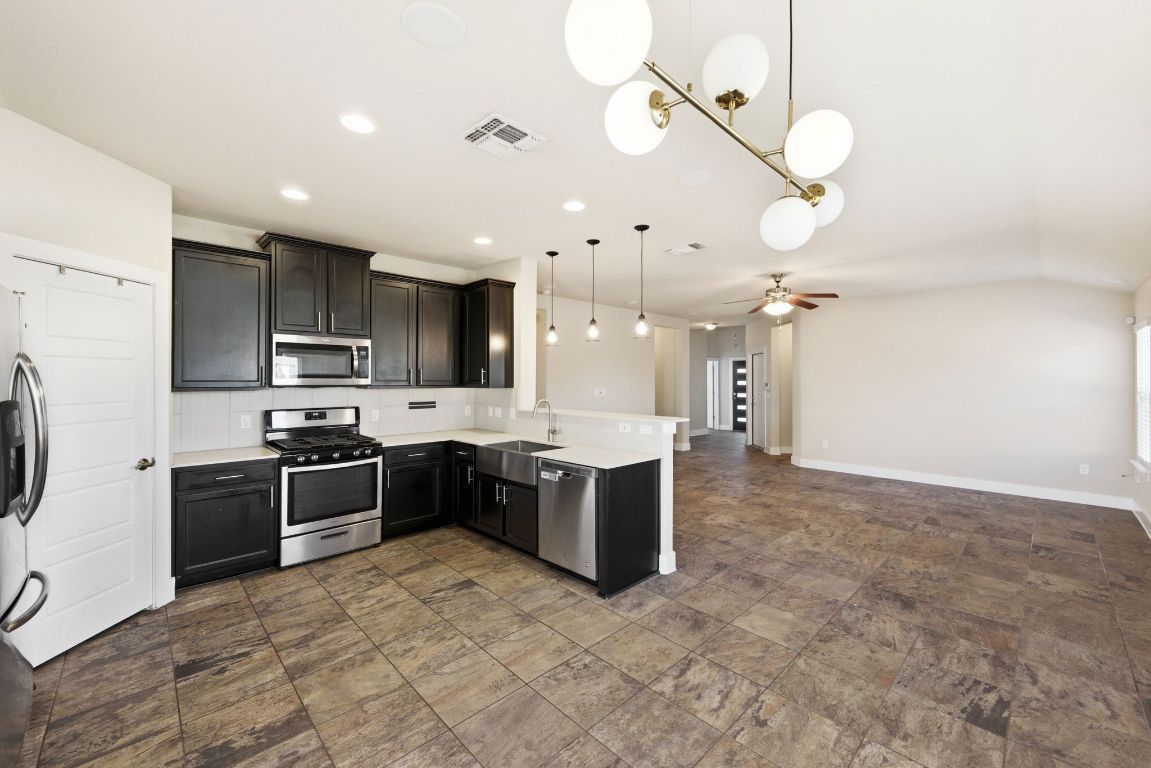 7013 Brick Slope Path Austin, TX 78744 - Photo 28 of 28 Kitchen with stainless steel appliances, pendant lighting, open floor plan, a peninsula, and dark cabinets