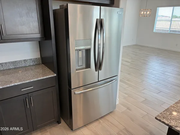 a view of a refrigerator in kitchen and an empty room with wooden floor
