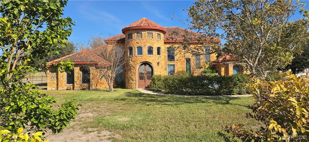 Mediterranean / spanish-style home featuring stone siding, a front yard, and a tile roof