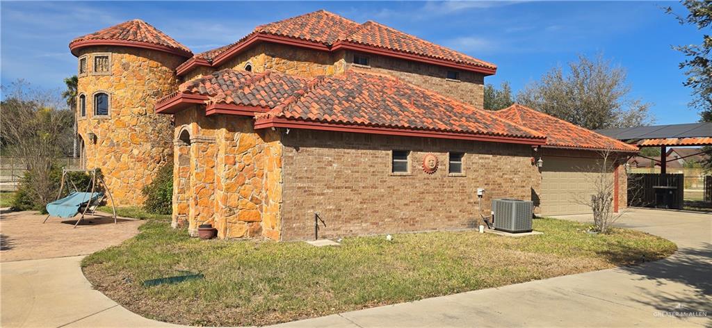 5312 Mile 4 Road Mission, TX 78573 - Photo 3 of 13 View of property exterior featuring driveway, a garage, stone siding, a lawn, and brick siding