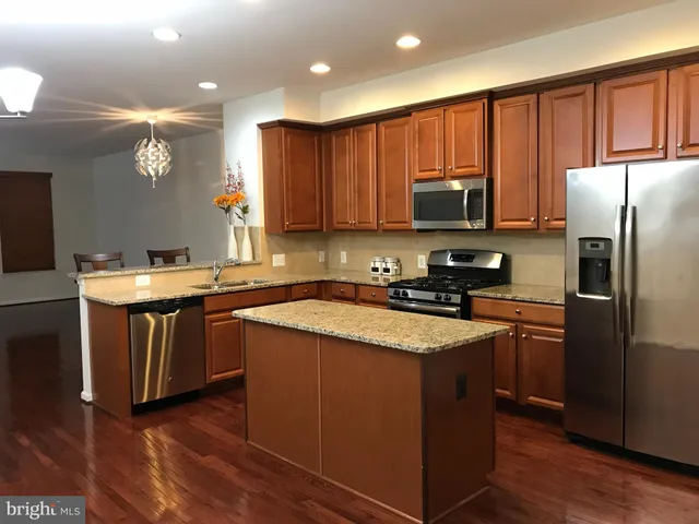 a kitchen with stainless steel appliances granite countertop a refrigerator a sink dishwasher a stove with wooden cabinets and floor