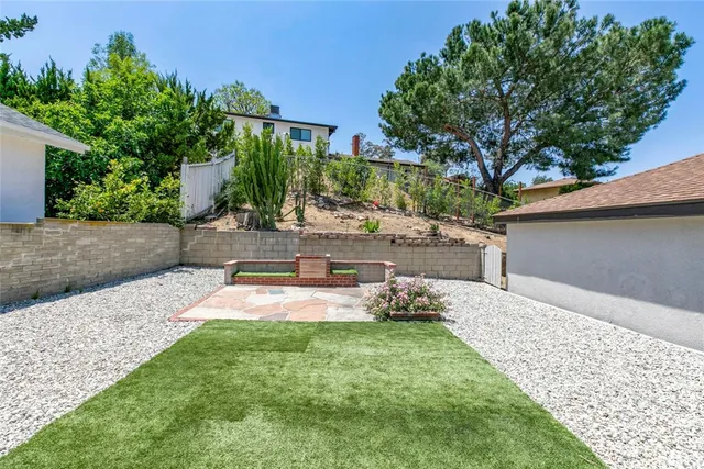 a backyard of a house with table and chairs plants and large tree