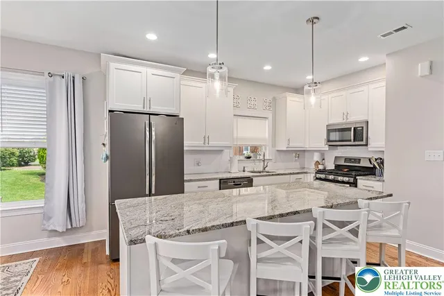 a kitchen with stainless steel appliances granite countertop a refrigerator a stove a sink a dining table and chairs with wooden floor