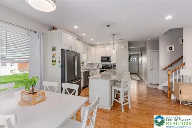 a kitchen with stainless steel appliances kitchen island granite countertop a refrigerator a stove a sink a dining table and chairs with wooden floor