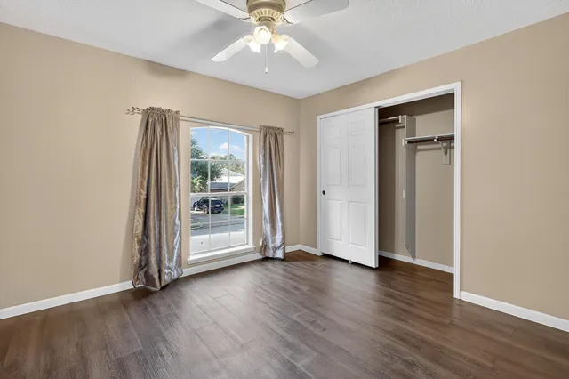 an empty room with wooden floor a ceiling fan and windows