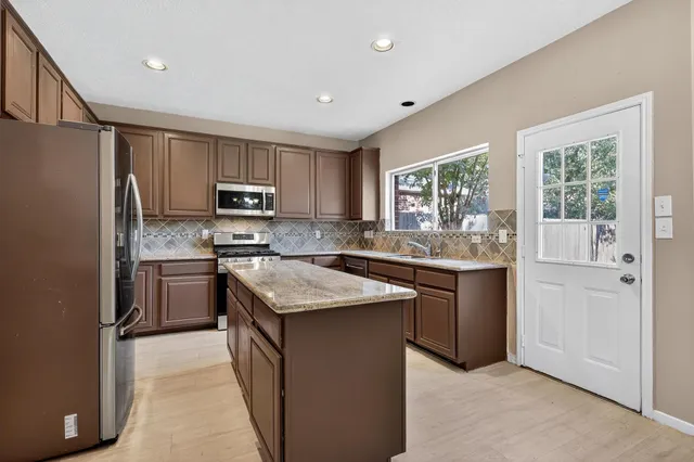 a kitchen with stainless steel appliances granite countertop a stove a sink dishwasher a refrigerator and a microwave oven with wooden cabinets