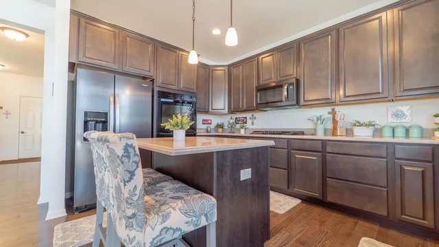 a kitchen with stainless steel appliances granite countertop a refrigerator a sink dishwasher a dining table and chairs with wooden floor