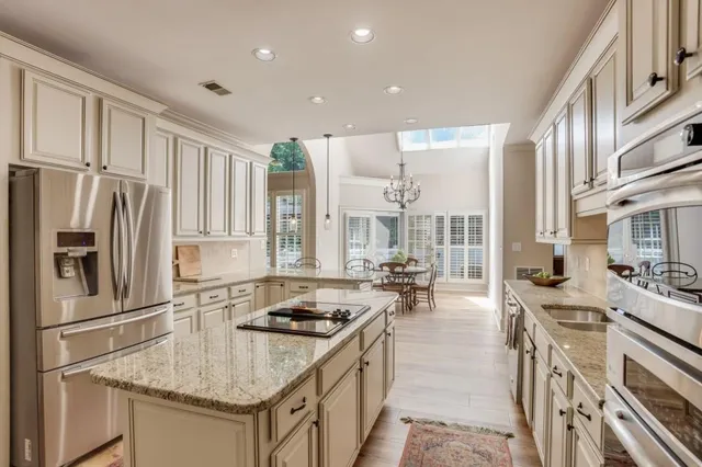 a kitchen with stainless steel appliances granite countertop a stove top oven a refrigerator a sink and white cabinets with wooden floor