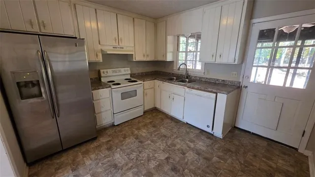 a kitchen with stainless steel appliances granite countertop a refrigerator a sink a stove a washer dryer and white cabinets