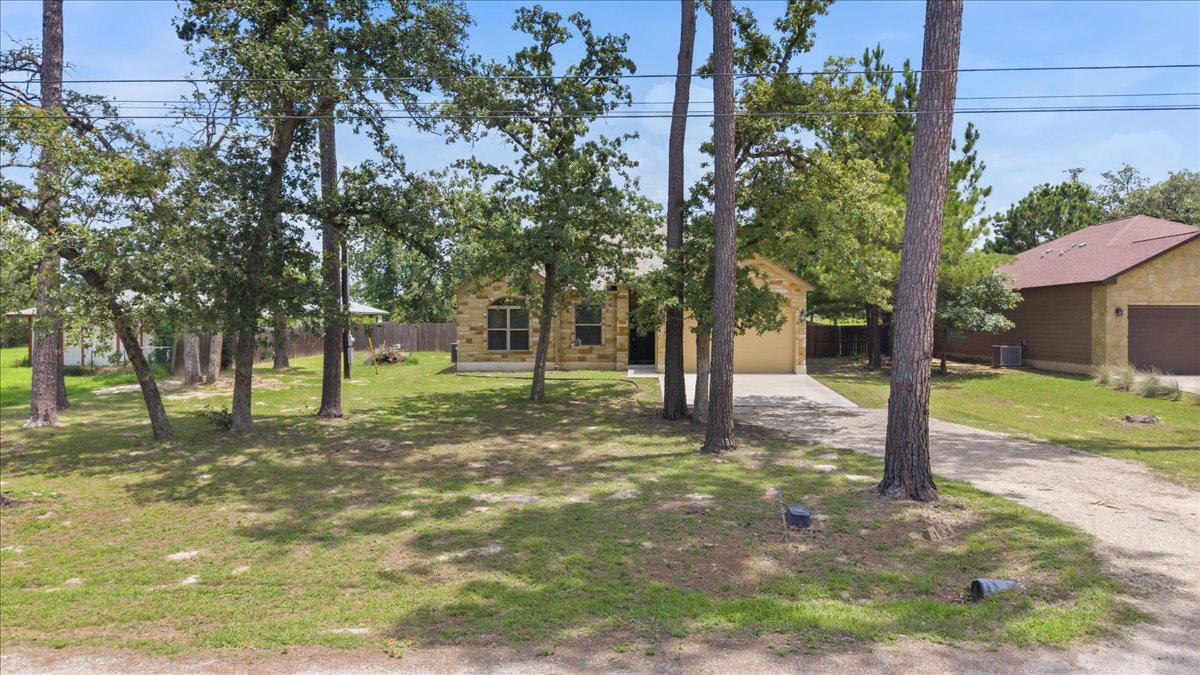 145 Cardinal Loop Paige, TX 78659 - Photo 5 of 40 Mature trees frame a charming stone-faced residence with an inviting driveway and a neatly kept front yard.