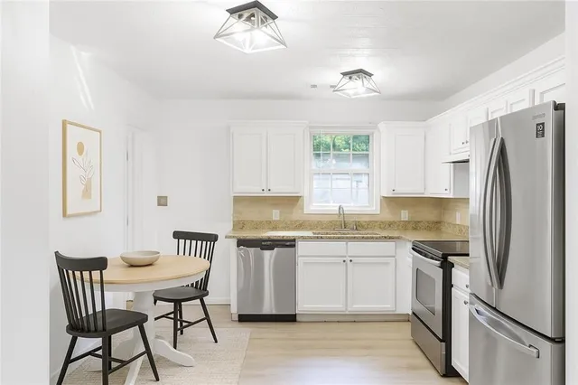 a kitchen with stainless steel appliances granite countertop a dining table chairs cabinets a sink and a window