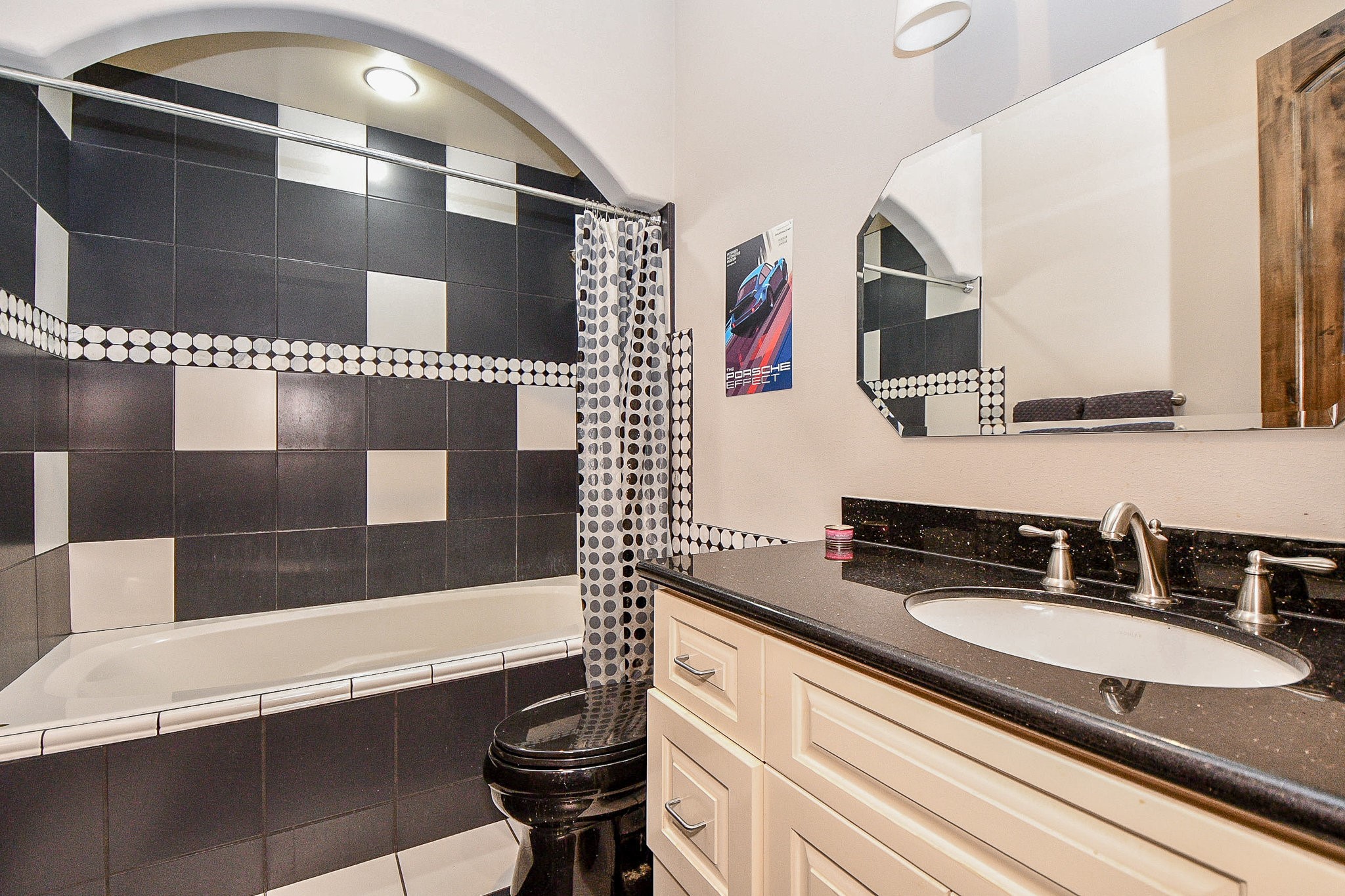 4119 Allen Street Houston, TX 77007 - Photo 40 of 50 Modern bathroom with a striking black and white tile design. Features a bathtub with an arched niche, a stylish vanity with a black countertop, and a sleek, polished faucet.