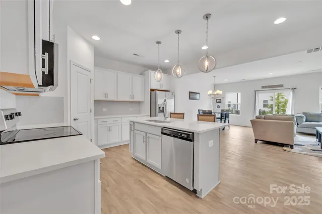 a kitchen with kitchen island a stove a sink a refrigerator and white cabinets with wooden floor