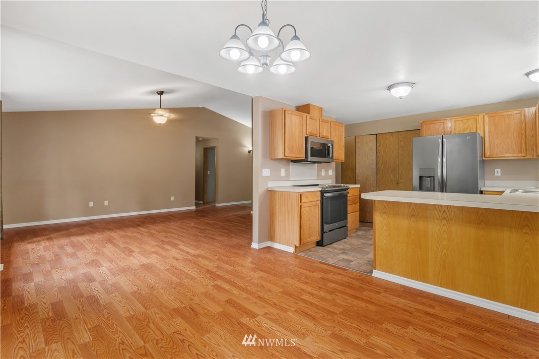 5418 187th Court Southwest Rochester, WA 98579 - Photo 5 of 24 a view of a kitchen with a sink a refrigerator a kitchen island wooden floor and a chandelier