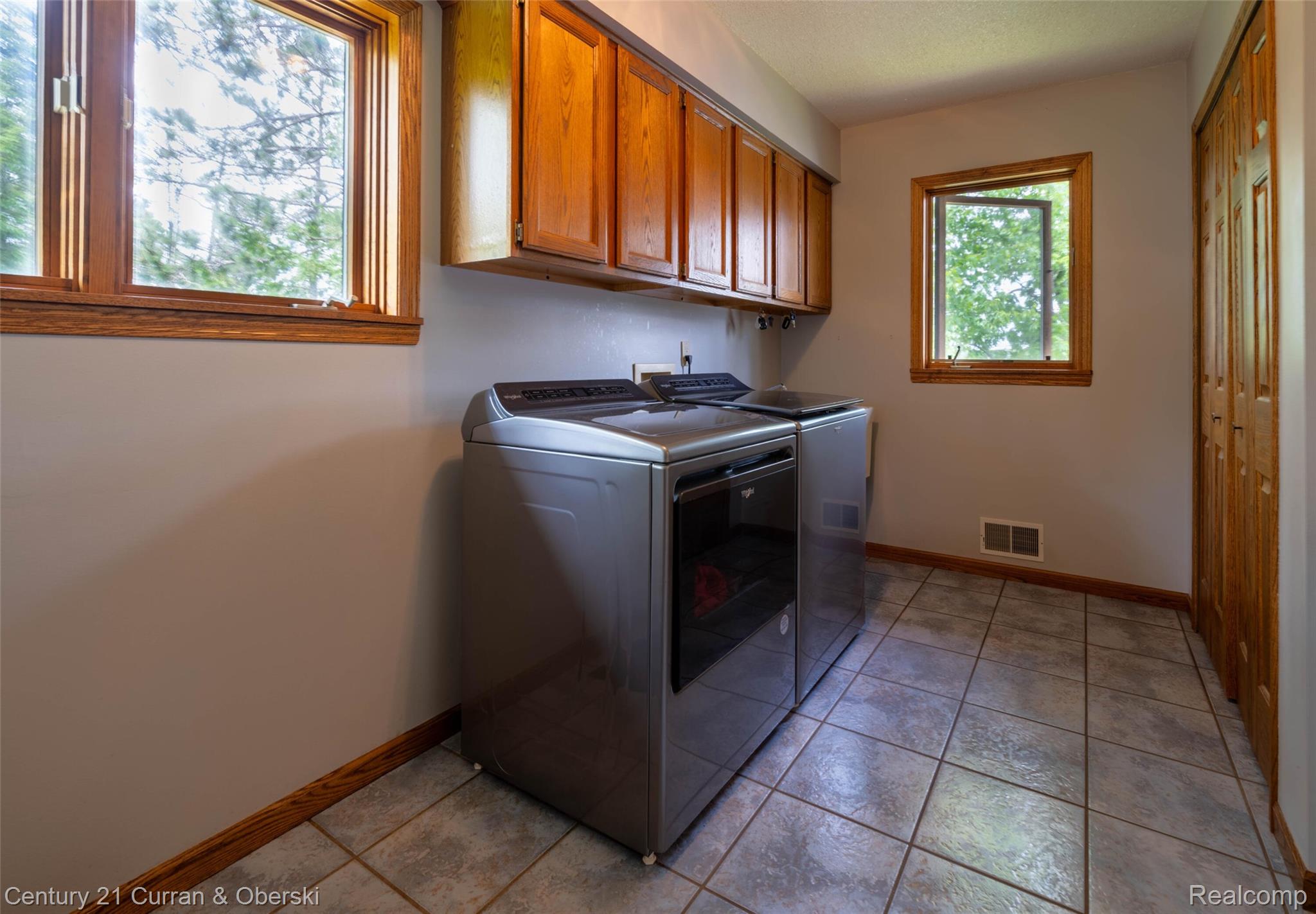 8775 Winding Rdg Drive Millersburg, MI 49759 - Photo 22 of 53 Dedicated laundry space featuring upper cabinetry, two windows with wood trim, neutral wall color, and tiled flooring