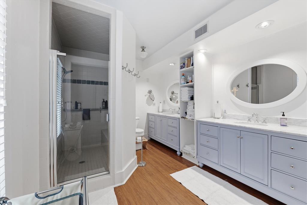 415 South Rice Street Hamilton, TX 76531 - Photo 13 of 28 Bathroom featuring a glass-enclosed shower, dual vanity with light blue cabinetry, granite countertops, oval mirrors, and wood-finish flooring