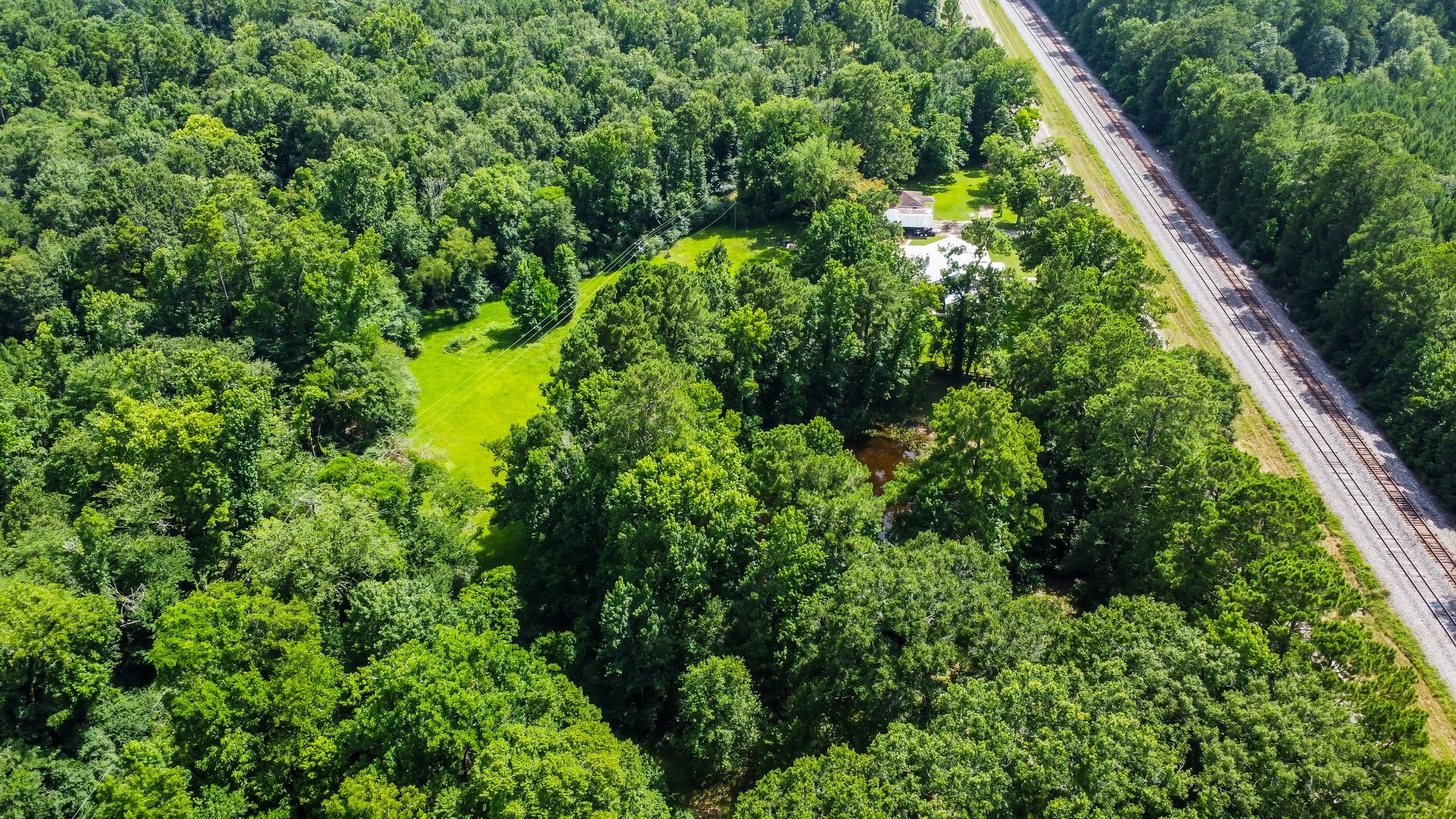 2446 Highway 116 Loop Livingston, TX 77351 - Photo 16 of 50 This aerial photo showcases a secluded property surrounded by lush forest, featuring a small clearing with a house. A railway line runs nearby, offering a mix of privacy and accessibility. Ideal for those seeking tranquility and nature.