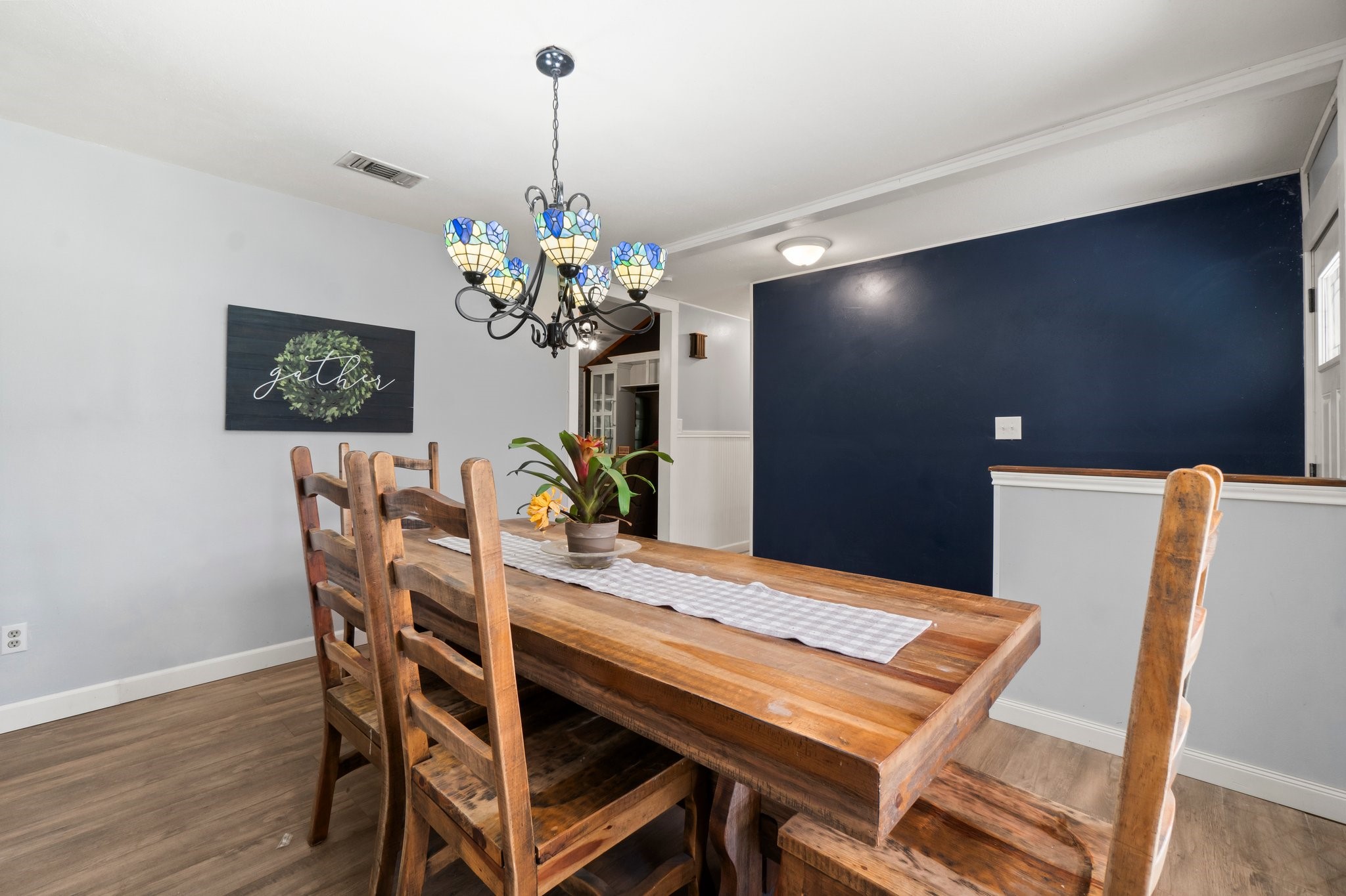 2446 Highway 116 Loop Livingston, TX 77351 - Photo 22 of 50 This dining area features a rustic wooden table with ladder-back chairs, a stylish stained glass chandelier, and a blue accent wall. The space is bright and inviting, perfect for gatherings.