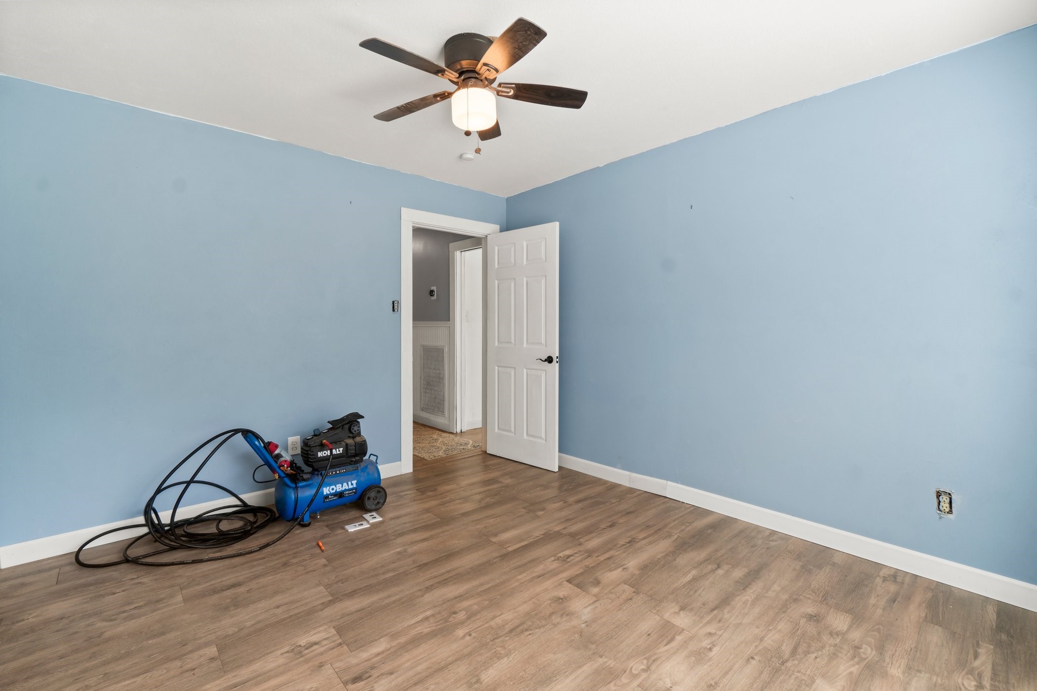2446 Highway 116 Loop Livingston, TX 77351 - Photo 31 of 50 This room features light blue walls, wood flooring, and a ceiling fan. It has a closet door and is currently unfurnished, offering a blank canvas for customization.