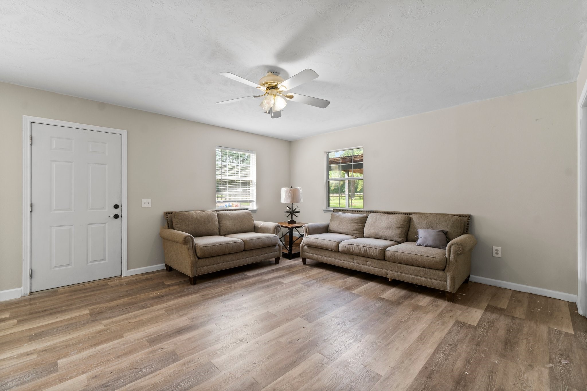 2446 Highway 116 Loop Livingston, TX 77351 - Photo 45 of 50 This living room features a cozy setup with two beige sofas on wood-style flooring, complemented by a ceiling fan. Natural light streams through two windows, creating a bright and inviting space.