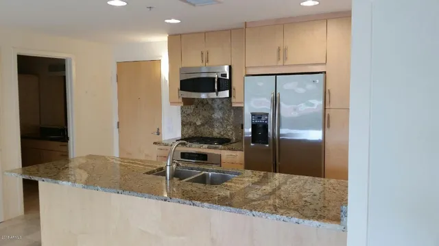 a kitchen with stainless steel appliances granite countertop a refrigerator a stove and a sink with wooden floor