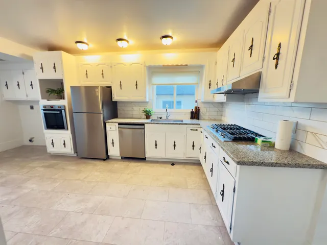 a large kitchen with stainless steel appliances granite countertop a stove a sink a refrigerator and white cabinets