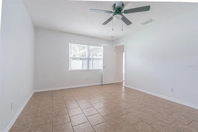 an empty room with chandelier fan and windows