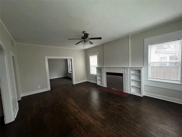 an empty room with wooden floor fireplace and windows