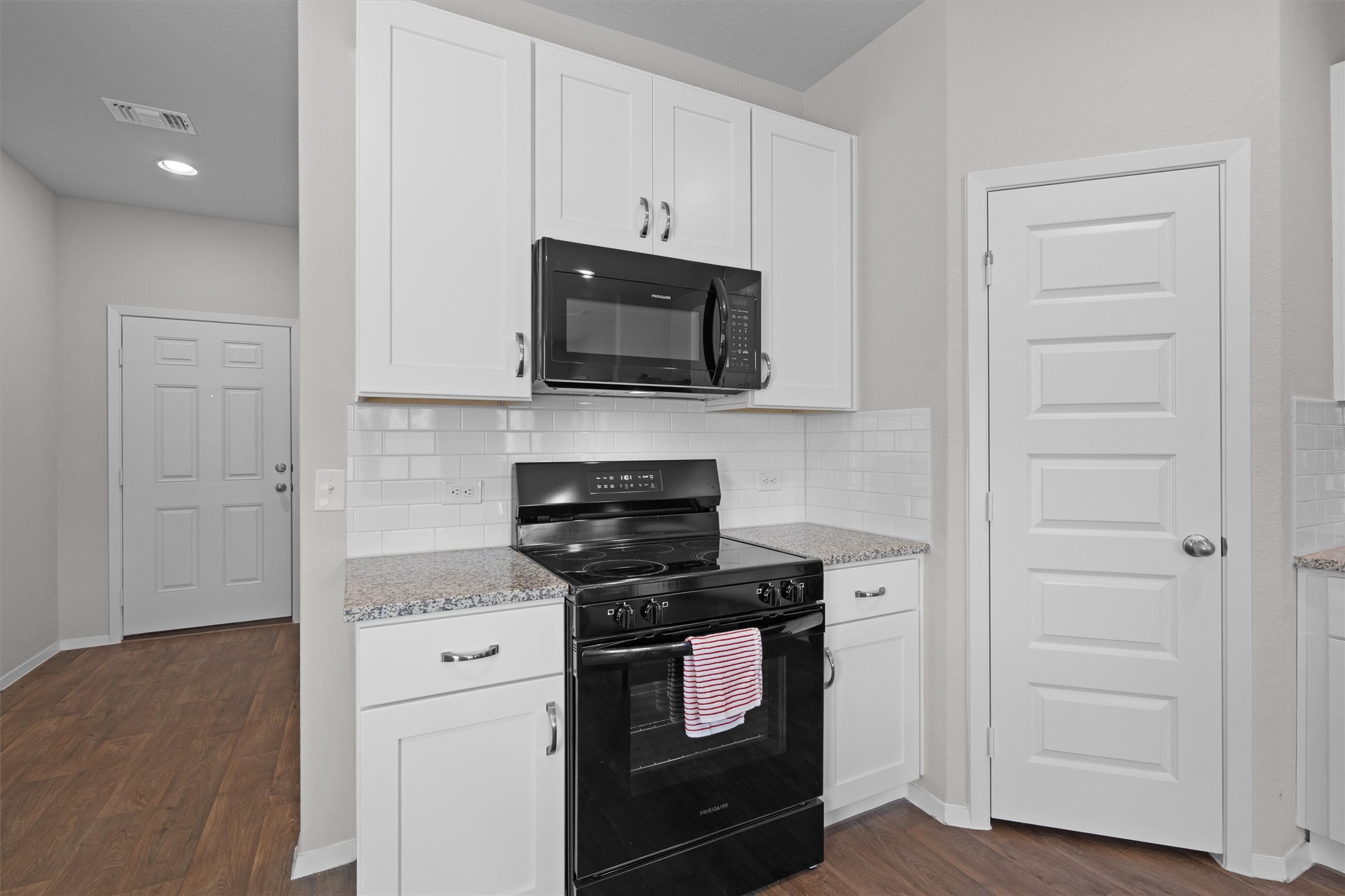 2606 Totley Road Manor, TX 78653 - Photo 9 of 28 a kitchen with stainless steel appliances granite countertop white cabinets and black stove top oven with wooden floor