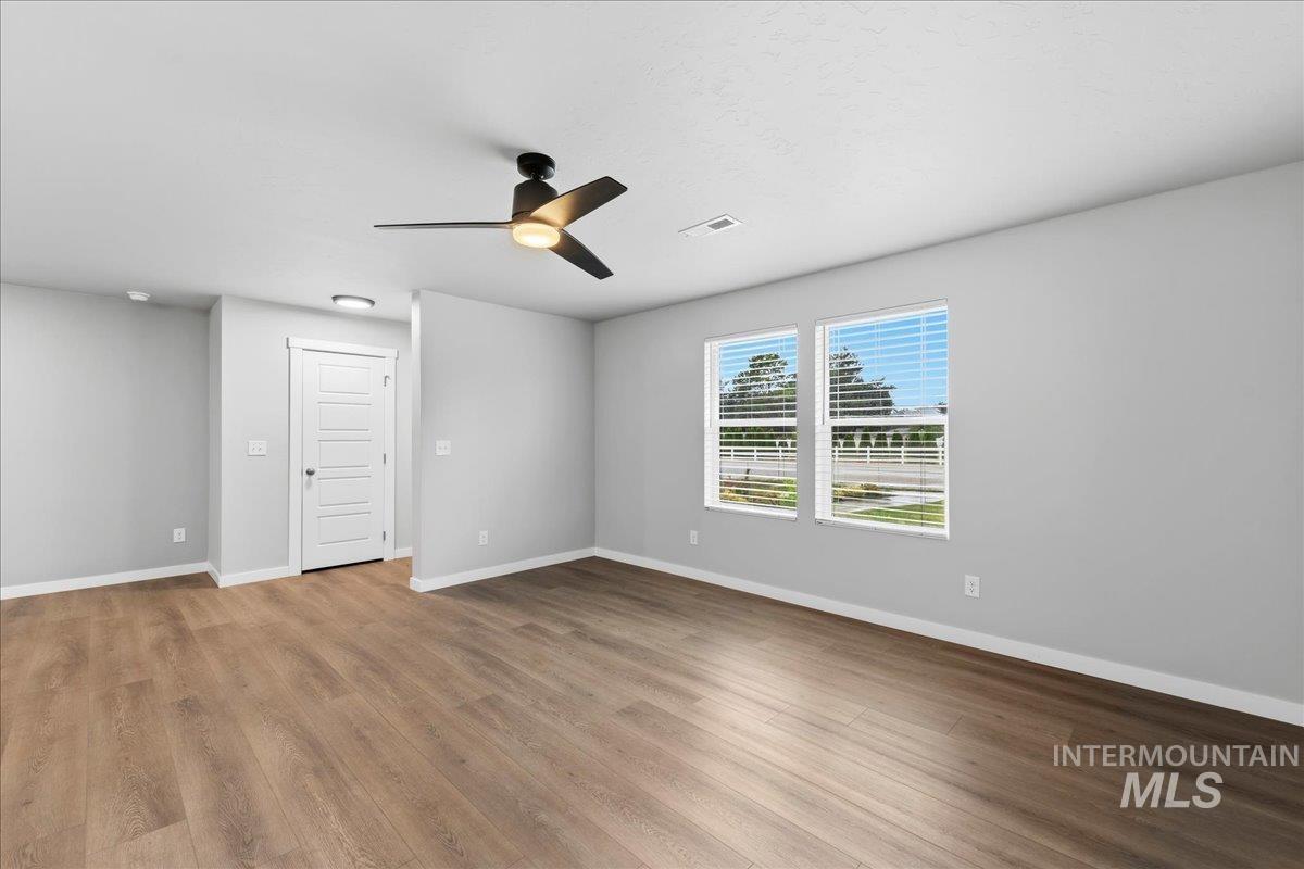 12475 West Victory Road Boise, ID 83709 - Photo 6 of 26 Spacious room featuring wood-finish flooring, light gray walls, white trim, two large windows with blinds, and a black ceiling fan with integrated lighting