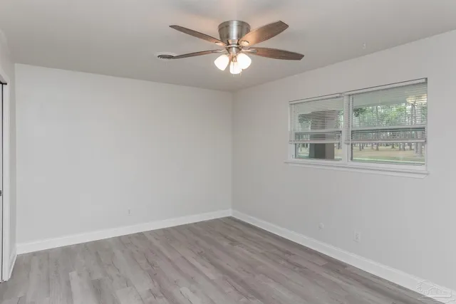 a view of an empty room with wooden floor and a ceiling fan