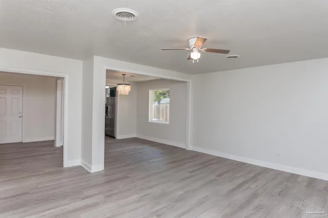 an empty room with wooden floor chandelier fan and windows