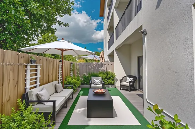 a view of a patio with couches table and chairs under an umbrella with a garden