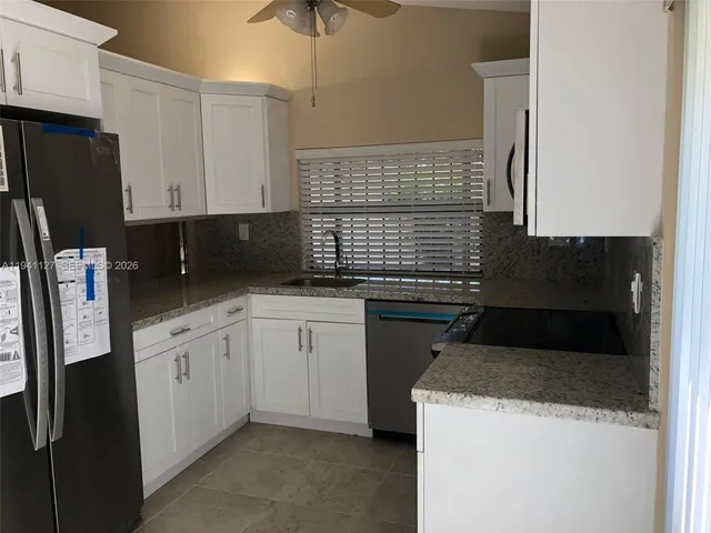 a kitchen with granite countertop a refrigerator a sink a stove and white cabinets