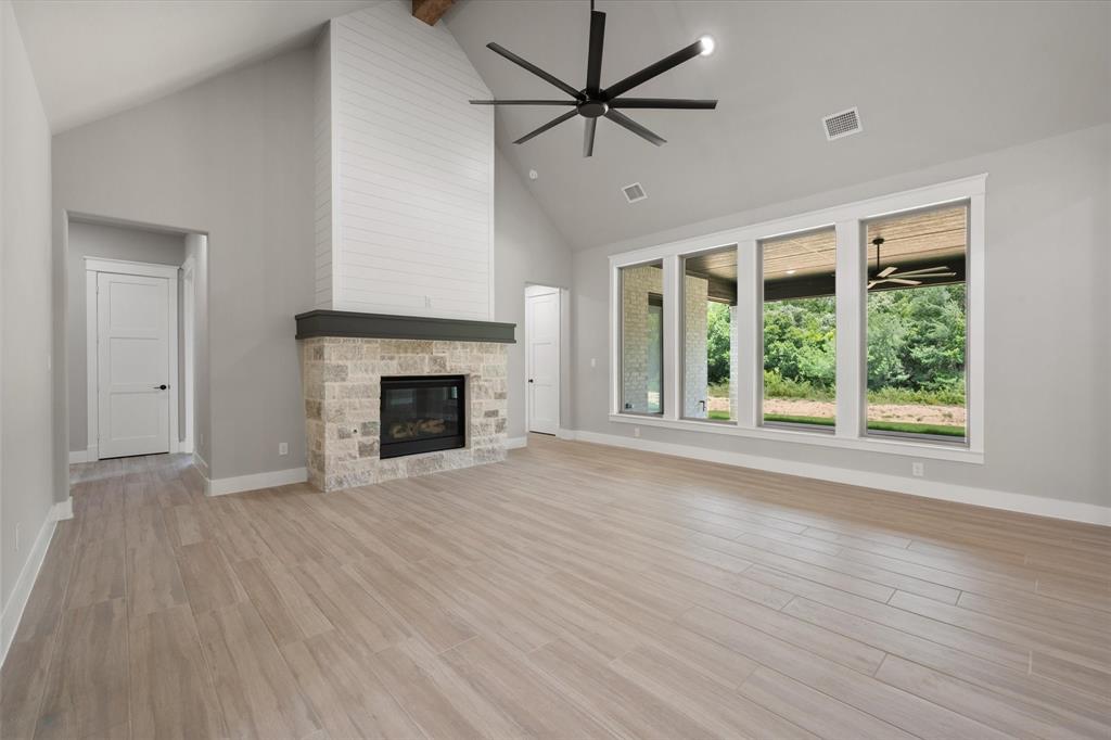 6610 Waggoner Way Midlothian, TX 76065 - Photo 8 of 40 Spacious living area featuring a vaulted ceiling, wood-finish flooring, and a stone fireplace with a shiplap surround
