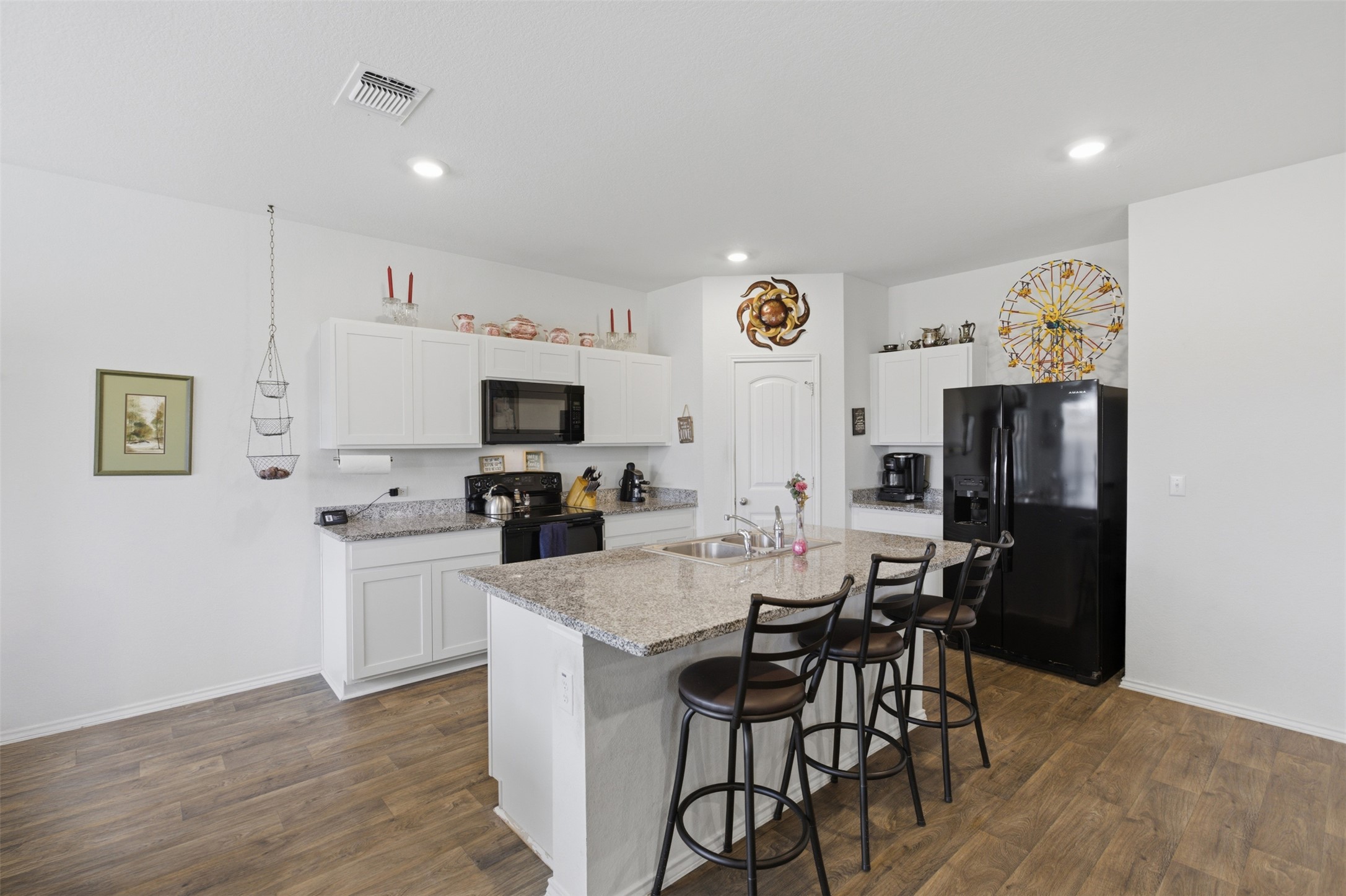 19017 Romano Drive Elgin, TX 78621 - Photo 15 of 33 Kitchen featuring an island with seating, white cabinetry, integrated black appliances, granite countertops, and wood-finish flooring