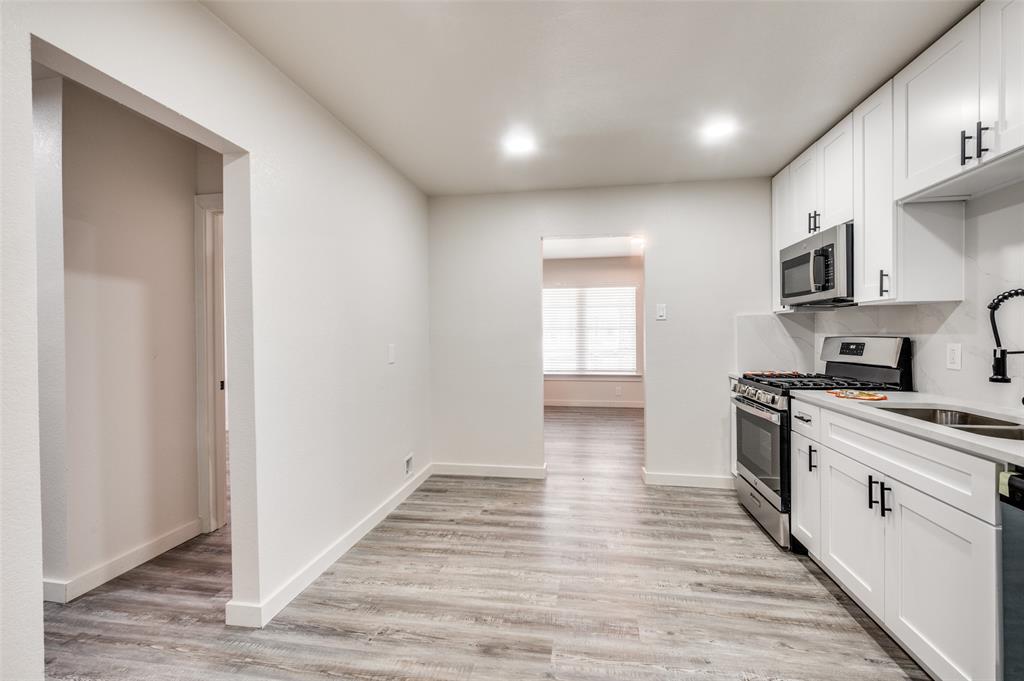 733 Southeast 3rd Street Grand Prairie, TX 75051 - Photo 9 of 24 Kitchen with white cabinets, appliances with stainless steel finishes, light wood-style floors, and light stone counters