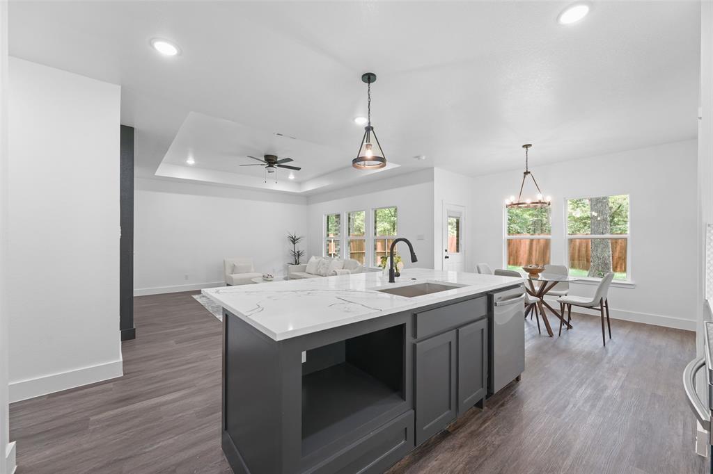 122 East Beachwood Loop Trinidad, TX 75163 - Photo 13 of 35 Open-concept living space featuring a central kitchen island with a quartz countertop and integrated sink, pendant lighting, wood-finish flooring, and ample natural light from multiple windows