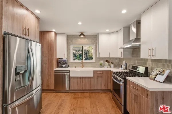 a kitchen with stainless steel appliances granite countertop a refrigerator a sink dishwasher a stove and white countertops with wooden floor