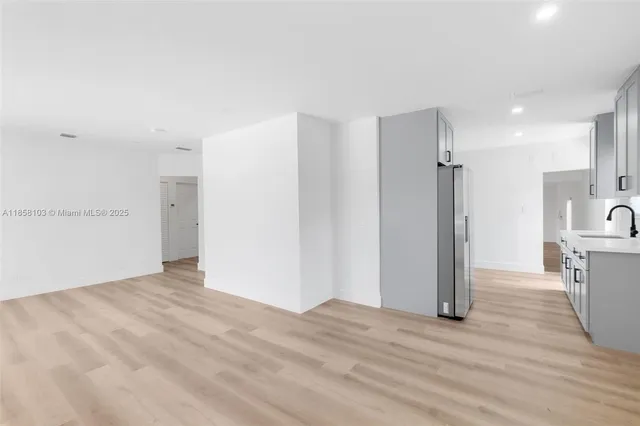 a view of an empty room with wooden floor and a kitchen